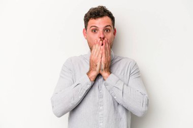 Beyaz arka planda izole edilmiş genç beyaz adam elleriyle ağzını kapatırken şok oldu..