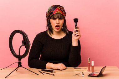 Makyaj öğretmeni olan genç bir kadın pembe arka planda izole edilmiş çok sinirli ve agresif çığlıklar atıyor..