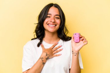 Pembe arka planda izole edilmiş bir araba tutan Latin kökenli genç kadın kahkahalar atıyor..