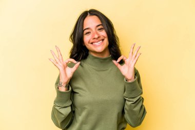 Sarı arka planda izole edilmiş genç İspanyol kadın neşeli ve kendinden emin, iyi bir hareket gösteriyor..