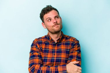 Kafkasyalı genç adam mavi arka planda izole edilmiş hedeflerine ve amaçlarına ulaşma hayali kuruyor.