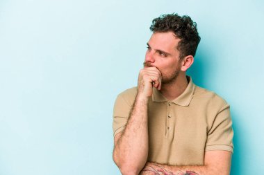 Mavi arka planda izole edilmiş genç beyaz adam rahatlamış bir şeyin fotokopi odasına baktığını düşünüyor..