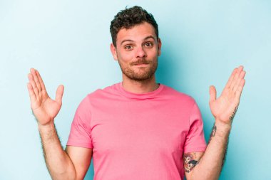 Kafkasyalı genç adam mavi arka planda izole edilmiş. Elinde işaret parmaklarıyla küçük bir şey tutuyor, gülümsüyor ve kendinden emin..