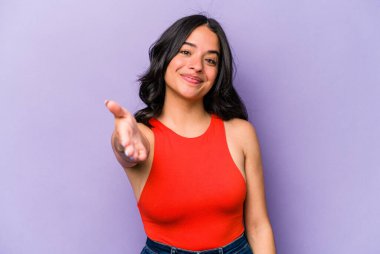 Mor arka planda izole edilmiş genç İspanyol kadın selamlama jesti olarak kameraya elini uzatıyor..