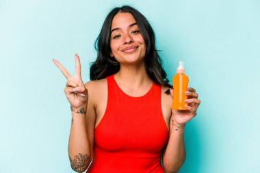 Mavi arka planda güneş kremi tutan genç İspanyol kadın iki numarayı parmaklarıyla gösteriyor..