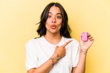 Pembe arka planda izole edilmiş anahtar taşıyan genç İspanyol kadın yan tarafı işaret ediyor.