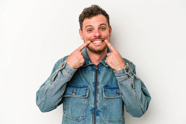 Beyaz arka planda izole edilmiş genç beyaz adam gülümsüyor, parmaklarını ağıza doğrultuyor..