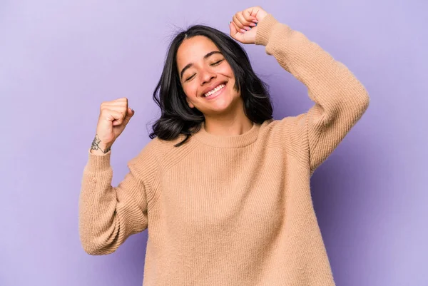 Mor arka planda izole edilmiş genç İspanyol kadın özel bir günü kutluyor, atlıyor ve enerjiyle kollarını kaldırıyor..