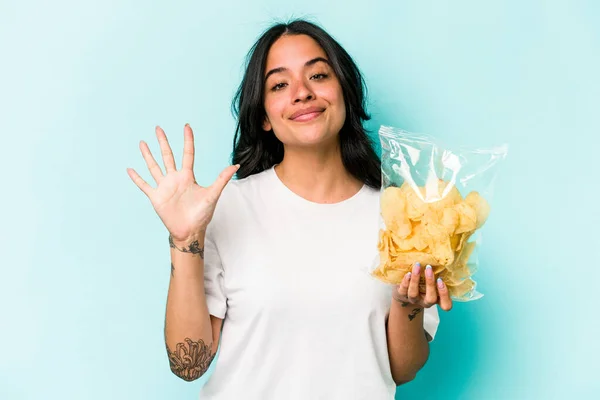 Ung Latinamerikansk Kvinna Håller Påse Chips Isolerad Blå Bakgrund Ler — Stockfoto