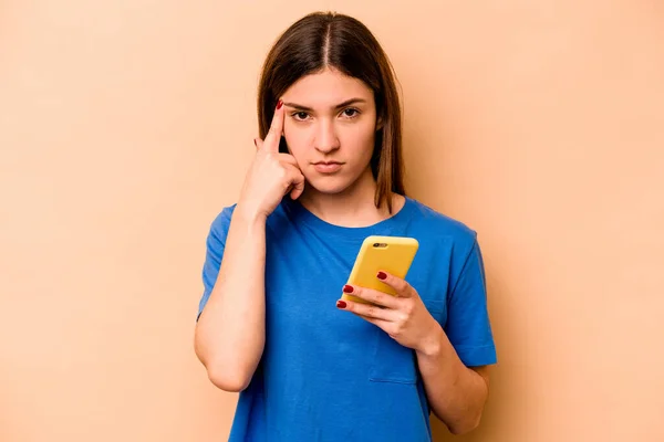 Ung Kaukasisk Kvinna Som Håller Mobiltelefon Isolerad Beige Bakgrund Pekar — Stockfoto
