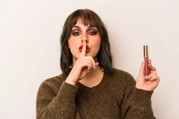 Beyaz arka planda izole edilmiş ruj tutan beyaz makyajcı genç kadın ya sır saklıyor ya da sessizlik istiyor..