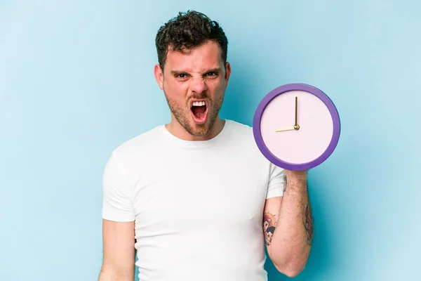 Young Caucasian Man Holding Clock Isolated Blue Background Screaming Very — Stock Fotó