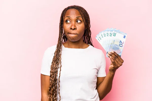 Молодая Афроамериканка Держащая Банкноты Розовом Фоне Замешательстве Чувствует Сомнение Неуверенность — стоковое фото