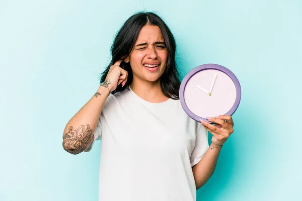 Young Hispanic Woman Holding Clock Isolated Blue Background Covering Ears — Stok fotoğraf