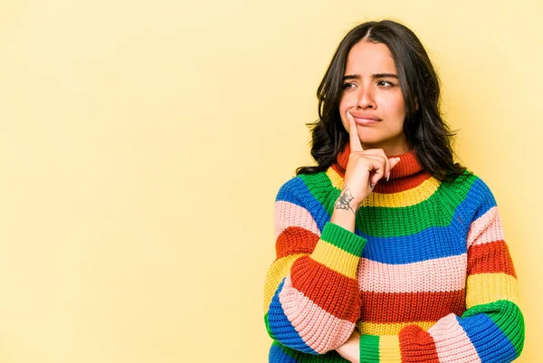 Sarı arka planda izole edilmiş genç İspanyol kadın şüpheli ve şüpheci bir ifadeyle yana bakıyor..