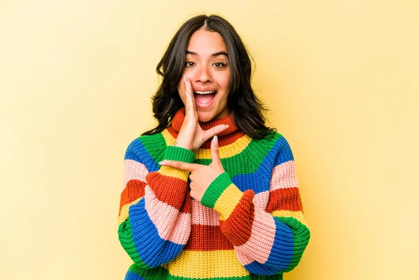 Latin kökenli genç bir kadın sarı arka planda izole edilmiş. Dedikodu yapıyor, bir şeyleri bildiriyor..