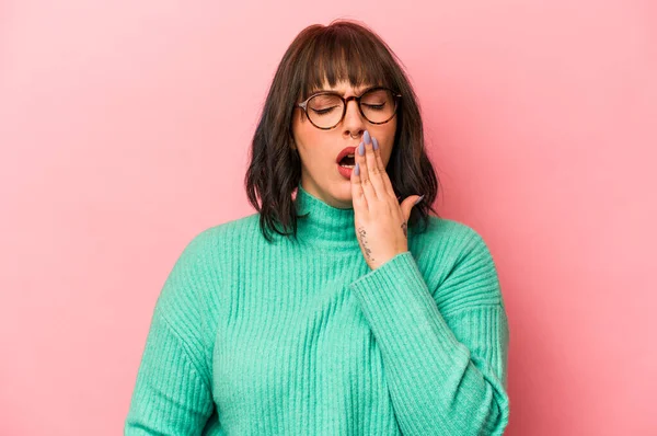 Pembe arka planda izole edilmiş genç beyaz kadın esniyor. Ağzı eliyle kapatan yorgun bir hareket sergiliyor..