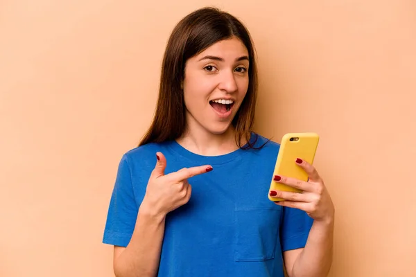 Молодая Кавказская Женщина Держит Мобильный Телефон Изолирован Бежевом Фоне — стоковое фото