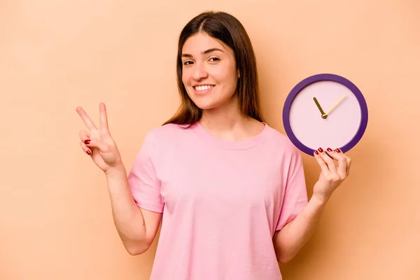 Joven Mujer Hispana Sosteniendo Reloj Aislado Sobre Fondo Beige Alegre —  Fotos de Stock