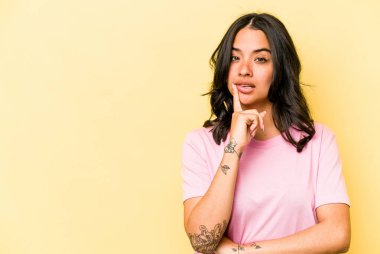 Sarı arka planda izole edilmiş genç İspanyol kadın şüpheli ve şüpheci bir ifadeyle yana bakıyor..