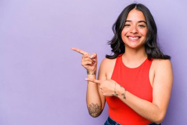 Mor arka planda izole edilmiş genç İspanyol kadın işaret parmaklarıyla işaret ederek heyecanlanıyor..