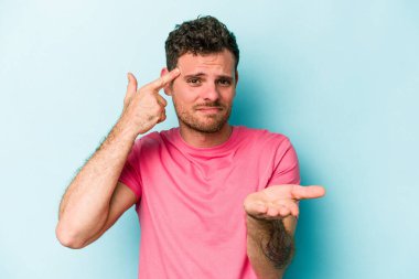 Kafkasyalı genç adam mavi arka planda izole edilmiş ve elinde bir ürün tutuyor..