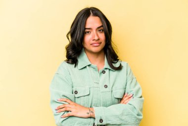 Sarı arka planda izole edilmiş genç İspanyol kadın şüpheli, belirsiz, seni muayene ediyor..