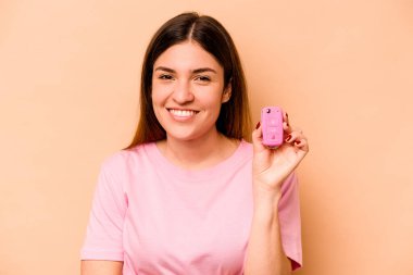 Latin kökenli genç bir kadın elinde bej arka planda izole edilmiş bir araba tutuyor. Gülüyor ve eğleniyor..