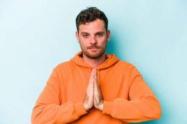 Kafkasyalı genç adam mavi arka planda izole edilmiş dua ediyor, bağlılık gösteriyor, dindar biri ilahi ilham arıyor..