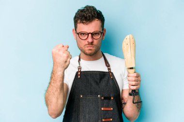 Kafkasyalı genç kunduracı, mavi arka planda izole edilmiş. Kameraya yumruk, agresif yüz ifadesi gösteriyor..