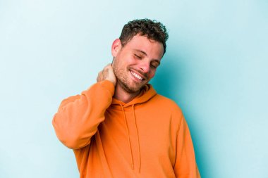 Kafkasyalı genç adam mavi arka planda izole edilmiş. Stres yüzünden boynu ağrıyor. Masaj yapıyor ve elle dokunuyor..