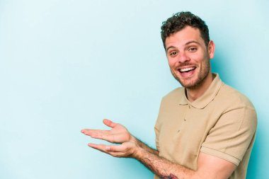 Mavi arka planda izole edilmiş genç beyaz bir adam palmiyesinde bir kopya alanı tutuyor..