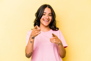 Sarı arka planda izole edilmiş genç İspanyol kadın parmaklarıyla ön tarafı işaret ediyor..