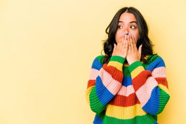 Genç İspanyol kadın sarı arka planda izole edilmiş. Düşünceli bir şekilde bir fotokopi odasına bakıyor. Ağzını eliyle kapatıyor..