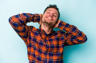 Kafkasyalı genç adam mavi arka planda izole edilmiş. Kendine güveniyor, elleri başının arkasında..