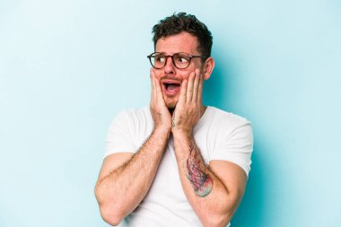 Kafkasyalı genç adam mavi arka planda izole edilmiş korkmuş ve korkmuş..