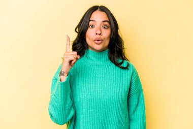 Sarı arka planda izole edilmiş, ağzı açık, üst tarafı işaret eden genç İspanyol kadın..