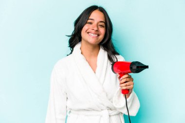 Mavi arka planda izole edilmiş, mutlu, gülümseyen ve neşeli bir kurutma makinesi tutan genç İspanyol kadın..