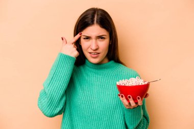 Latin kökenli genç bir kadın bej arka planda izole edilmiş mısır gevreği yerken işaret parmağıyla yaptığı hayal kırıklığını gösteriyor..