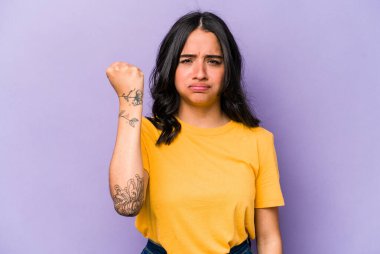 Mor arka planda izole edilmiş genç İspanyol kadın kameraya yumruğunu, agresif yüz ifadesini gösteriyor..