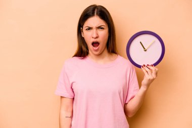 Elinde bej arka planda izole edilmiş bir saat tutan genç İspanyol kadın çok sinirli ve agresif bağırıyor..