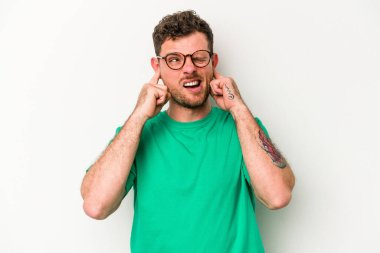 Beyaz arka planda izole edilmiş genç beyaz bir adam parmaklarıyla kulaklarını kapatıyor, gürültülü bir ortam yüzünden stresli ve çaresiz..