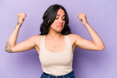 Mor arka planda izole edilmiş genç İspanyol kadın güçlü bir jest yapıyor, kadınsı gücün sembolü.