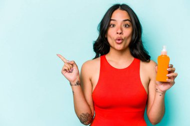 Mavi arka planda izole edilmiş güneş kremi tutan genç İspanyol kadın.