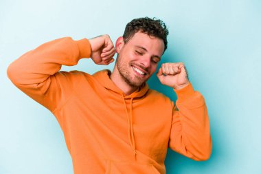 Mavi arka planda izole genç beyaz adam özel bir günü kutluyor, atlıyor ve enerjiyle kollarını kaldırıyor..