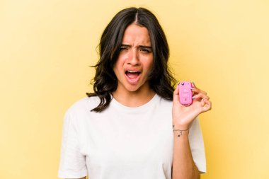 Pembe arka planda izole edilmiş anahtar taşıyan Latin kökenli genç bir kadın çok sinirli ve agresif bağırıyor..