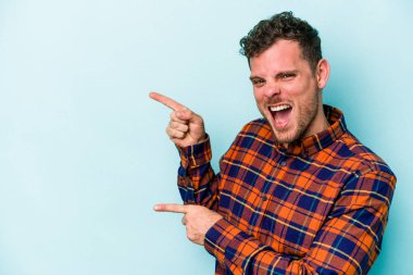 Mavi arka planda izole edilmiş genç beyaz adam işaret parmağıyla fotokopi alanını işaret ederek heyecan ve arzusunu ifade ediyor..