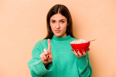 Latin kökenli genç bir kadın bej arka planda izole edilmiş mısır gevreği yiyor..