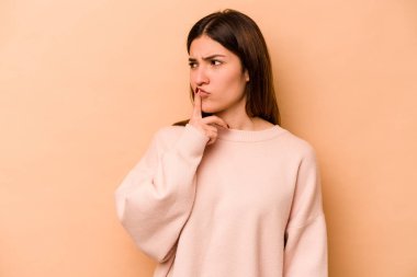 Genç İspanyol kadın bej arka planda izole edilmiş bir şekilde bir sır saklıyor ya da sessizlik istiyor..