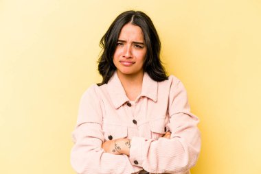 Sarı arka planda izole edilmiş, hoşnutsuzca kaşlarını çatan, kollarını kavuşturan genç İspanyol kadın..